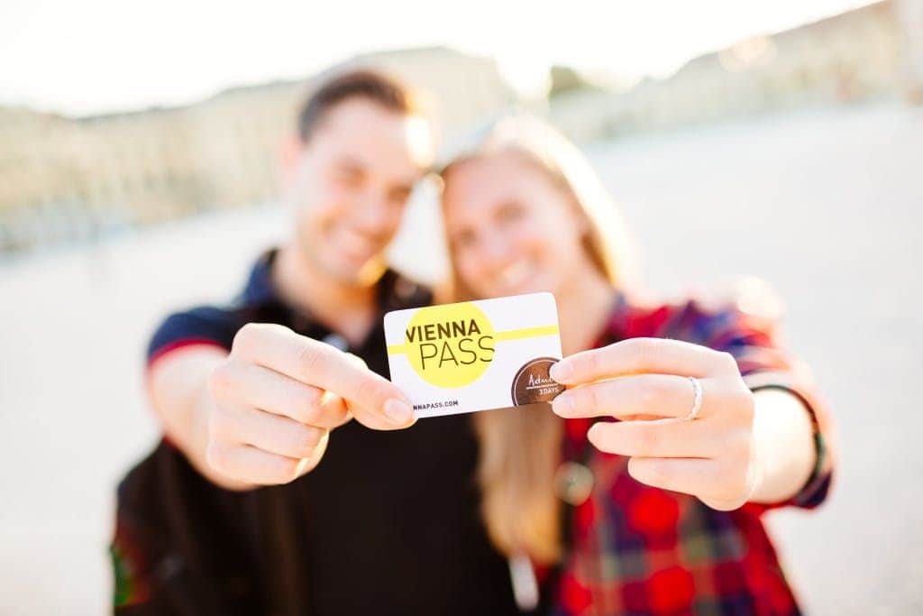 Vienna PASS: Admission to 90+ Attractions Two smiling people holding a Vienna Pass card, with blurred background indicating an outdoor setting.