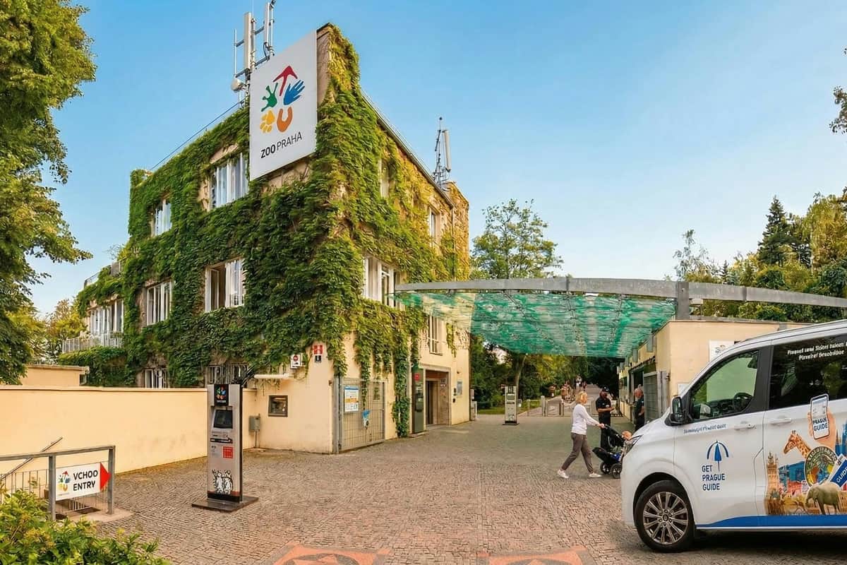 Prague Zoo: Roundtrip Transport + Audio Guide Entrance to Prague Zoo with a building covered in green ivy, a canopy structure, and visitors walking nearby.