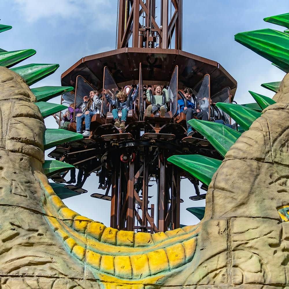 Chessington World of Adventures: Entry Ticket People ride a drop tower amusement ride, surrounded by large, decorative green spikes and stone structures under a blue sky.