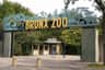 布朗克斯动物园（ Bronx Zoo ）的入口大门，上面有黄色的大字母。 后面可以看到绿叶和售票亭。